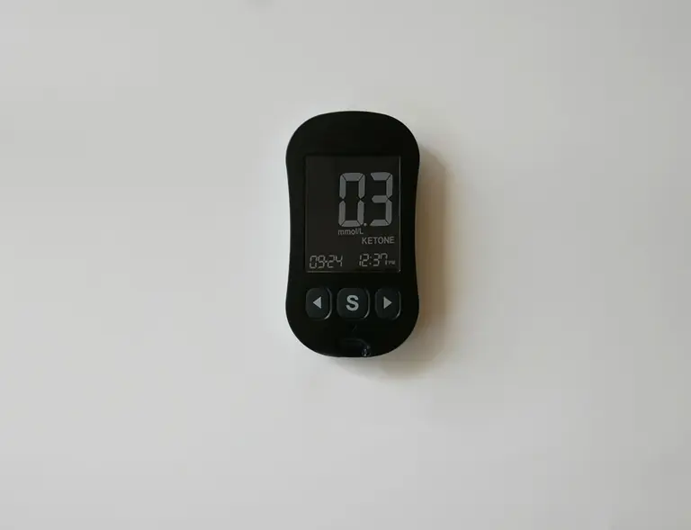 A close-up of a digital ketone meter displaying readings on a white surface.