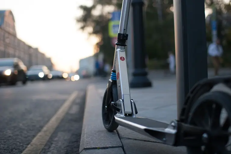 Close-up of a scooter parked on a busy city sidewalk at dusk.