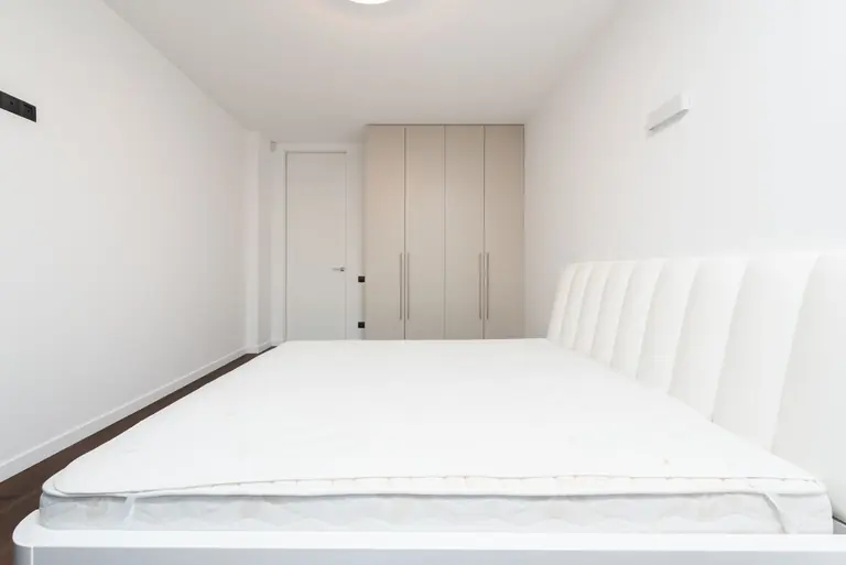 Contemporary minimalist bedroom featuring a white mattress and sleek wardrobe under soft lighting.
