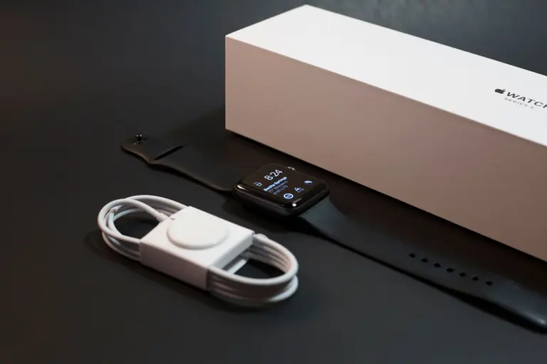 A modern smartwatch with charger displayed elegantly alongside its packaging on a dark surface.