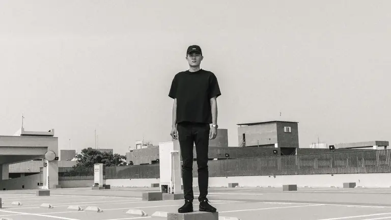 Black and white photo of a man in casual fashion on a rooftop parking lot.