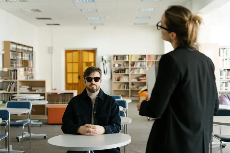 Blind student engaged in classroom discussion with teacher. Inclusive education setting.