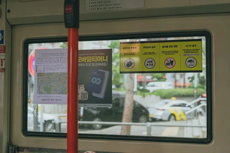 View from a Seoul city bus window, displaying local urban signs and ads.